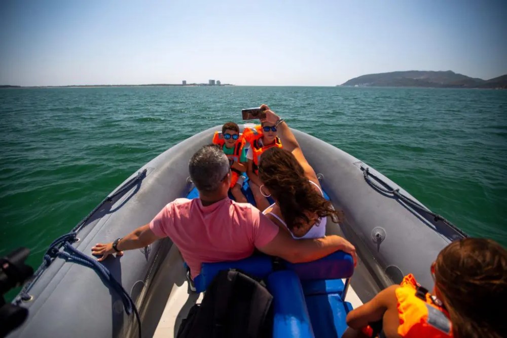 A family takes a selfie on a boat in the ocean, wearing life jackets.