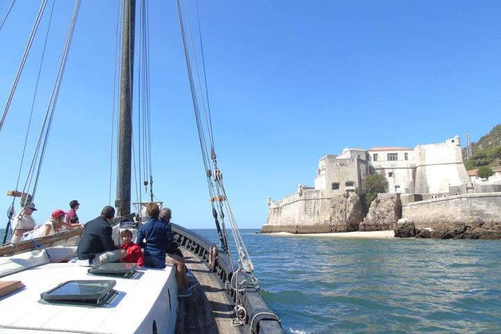 People on a sailboat approaching a coastal fort on a sunny day.