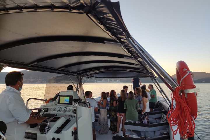 Group of people on a boat at sunset, with a person steering near the control panel.