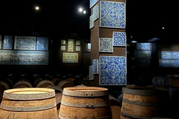 Dim room with wooden barrels and decorative blue patterned tiles on walls.