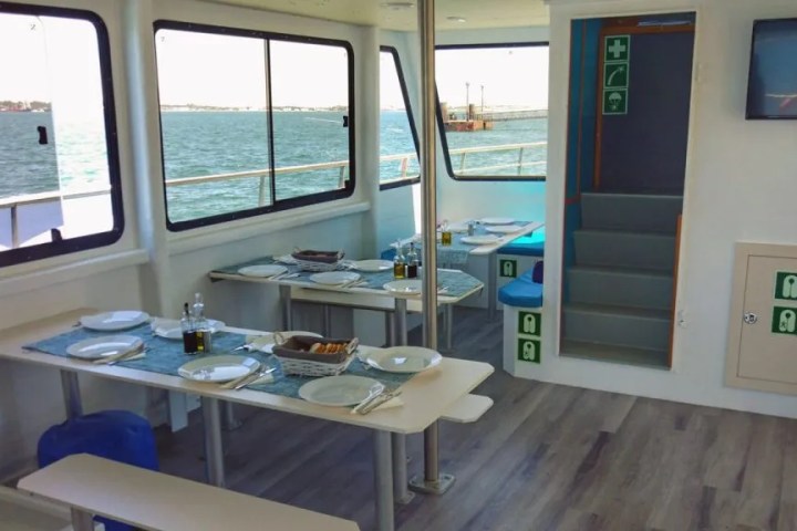 Boat cabin with set dining tables by windows and emergency signs.