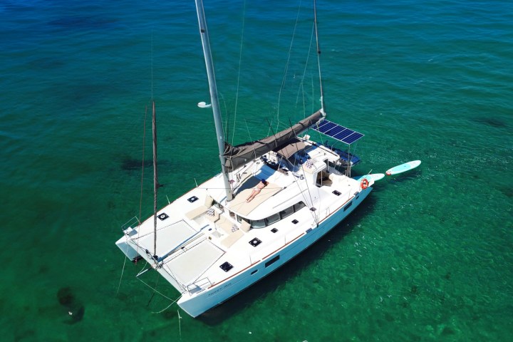 A white catamaran with solar panels floats on clear blue water.