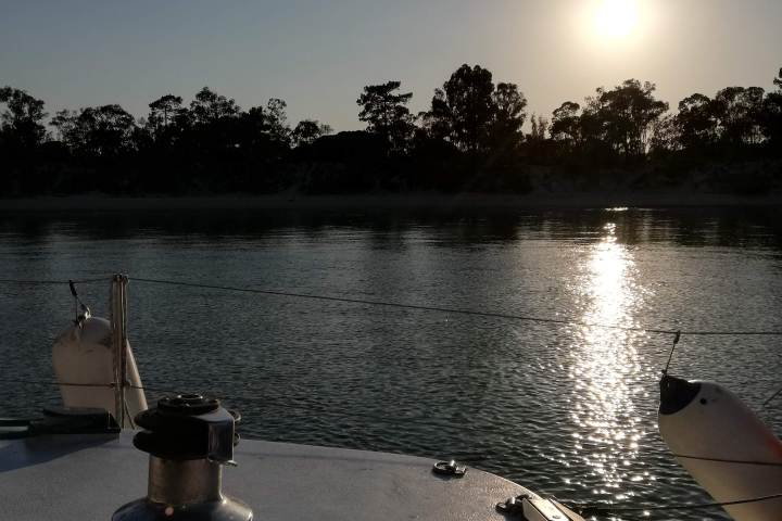 Sunset over a calm lake, viewed from a boat with trees silhouetted on the horizon.