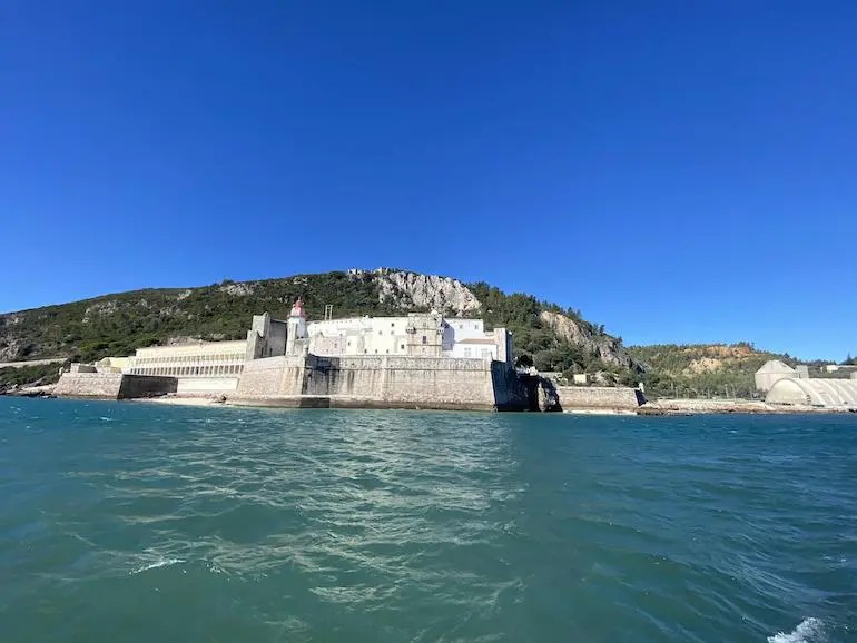 Fortress by the sea with a hill in the background under a clear blue sky.
