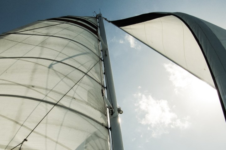 View looking up at white sails of a boat against a blue sky with scattered clouds.