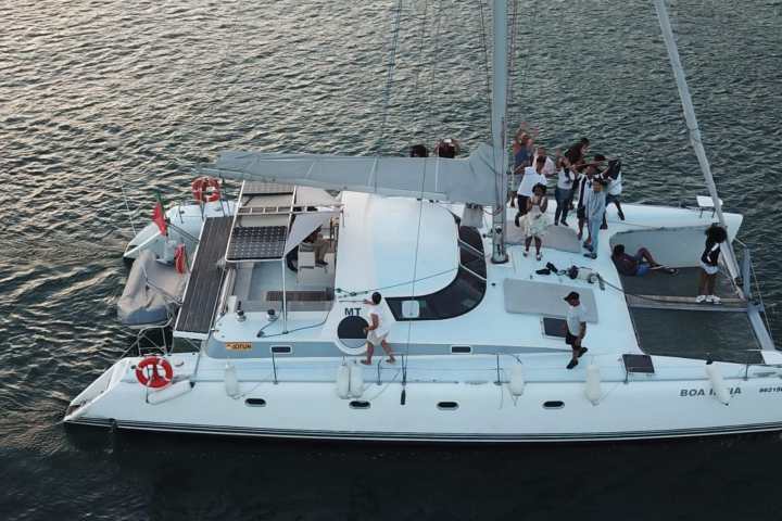 Aerial view of people on a white catamaran sailing on calm water.