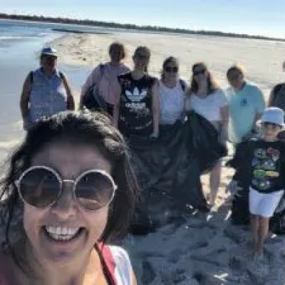 Group of people on a sunny beach, one taking a selfie.