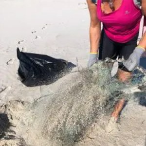 Person cleaning beach, holding a fishing net, with a trash bag nearby.