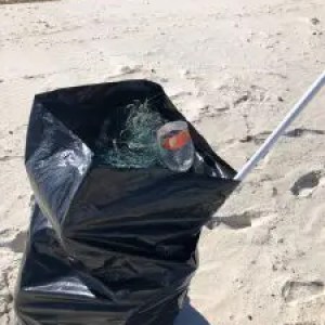 Trash bag on sandy beach containing litter, including a plastic cup.