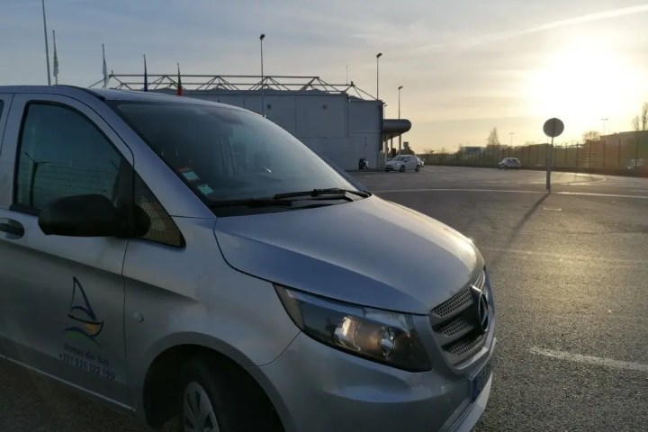 Silver van in parking lot at sunset with building in background.