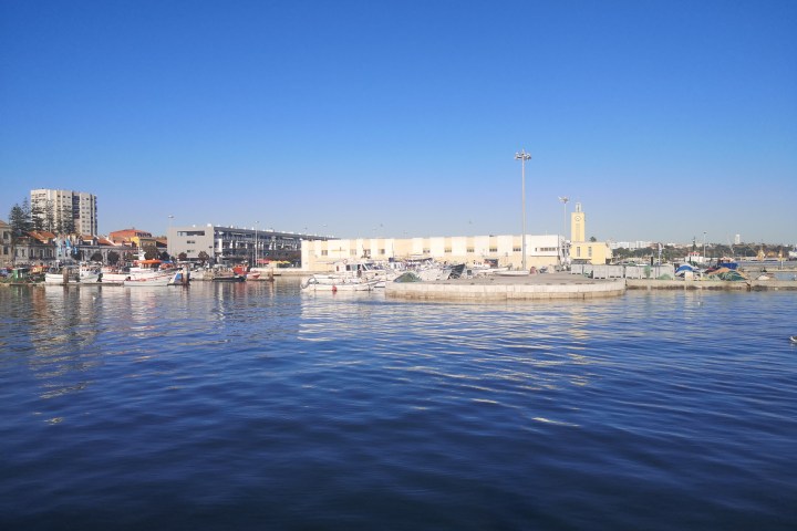 Clear blue sky over a calm harbor with boats and buildings.