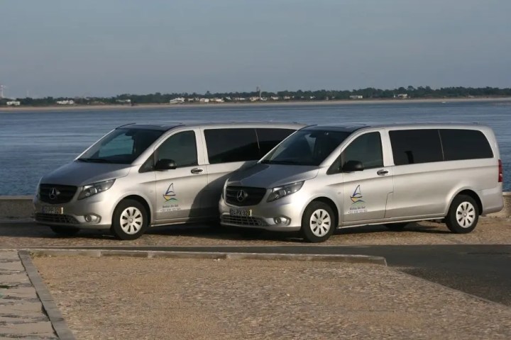 Two silver vans with logos parked near a waterfront.