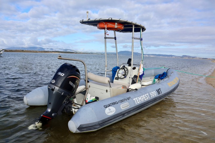 Inflatable boat with motor docked on sandy shore under cloudy sky.