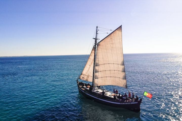 Sailing ship with a flag on calm blue sea under clear sky.