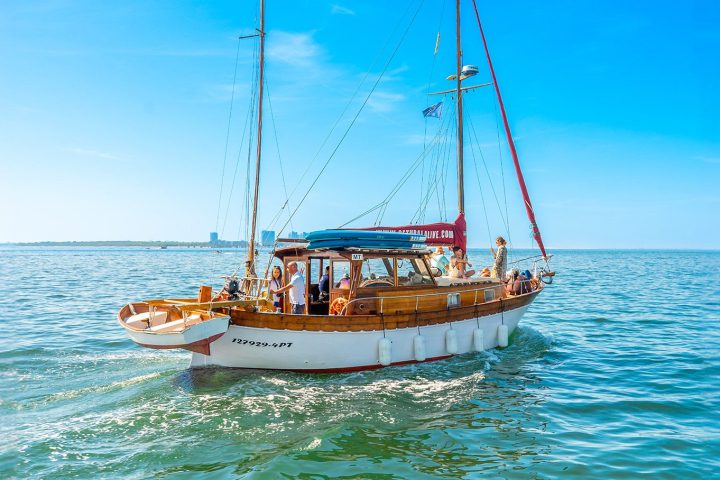 Vintage wooden sailboat sailing on a calm sea under a clear blue sky.