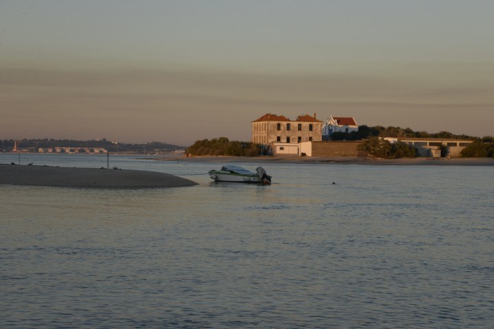 Small boat on calm water near an island with a few buildings at sunset.
