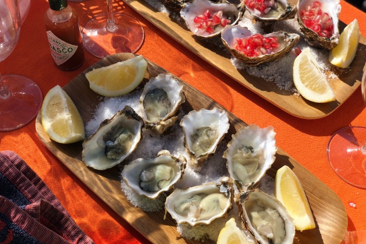 Oysters on wooden platters with lemon wedges and diced toppings.