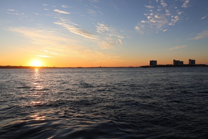 Sunset over the ocean with city skyline and clouds.