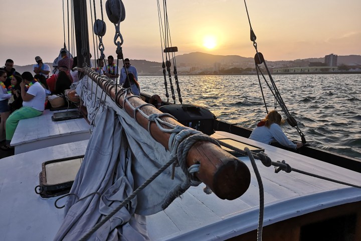 People on a sailboat at sunset with mountains in the background.
