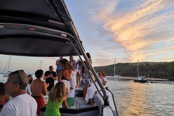 People enjoying a sunset boat party, with sailboats in the background.