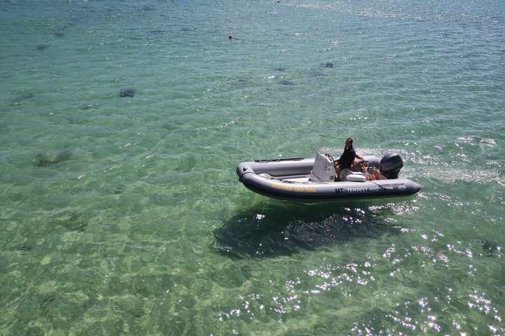 Person in a small motorboat on clear green water with other boats in the background.