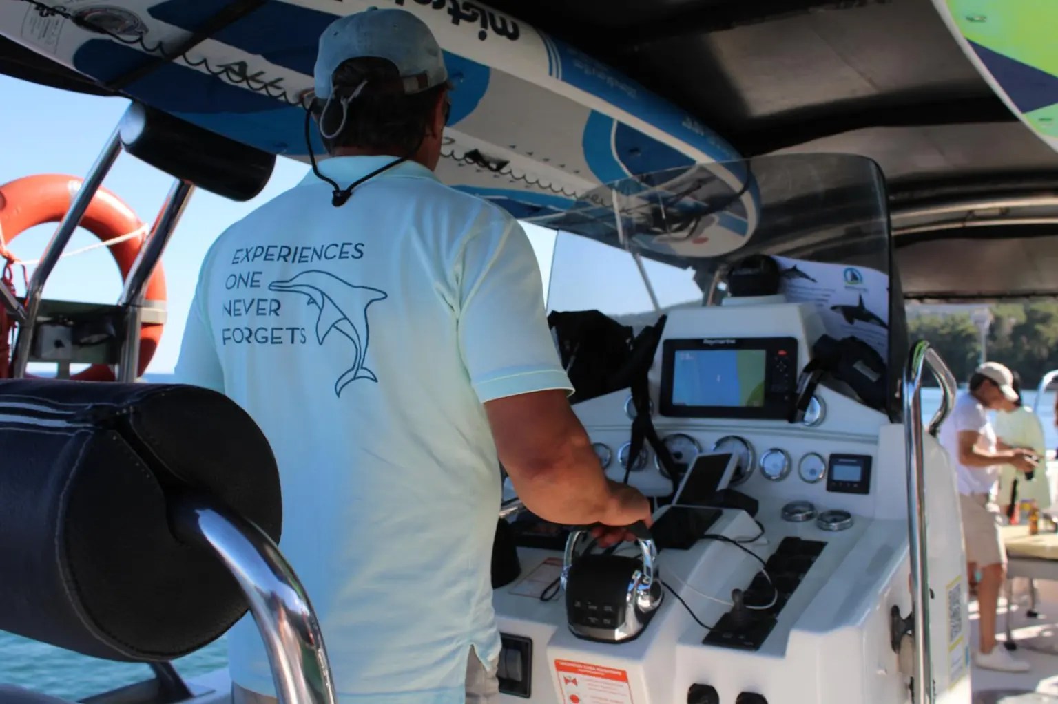 Person steering a boat with surfboards and ocean view in background.