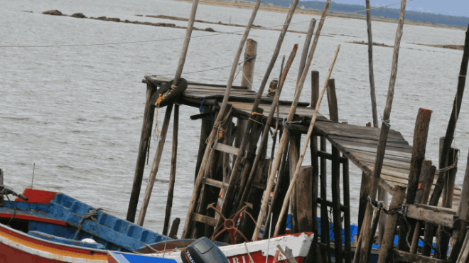 Small red boat docked at a wooden pier over calm water.