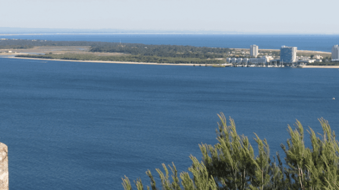 Coastal view with blue ocean, distant peninsula, and old stone building on the left.