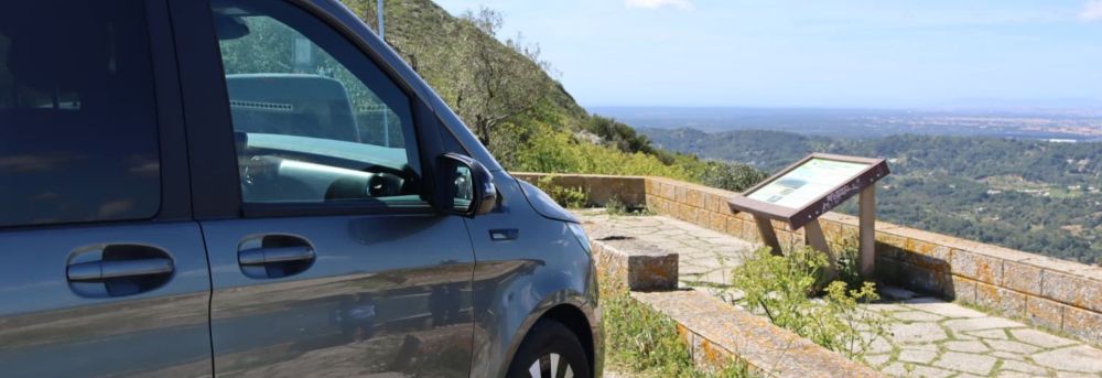 Car parked at scenic overlook with hills and city view in background.