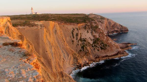 Lighthouse on a cliff by the sea at sunset.