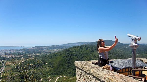 Woman taking a selfie on a viewpoint overlooking a vast hilly landscape.