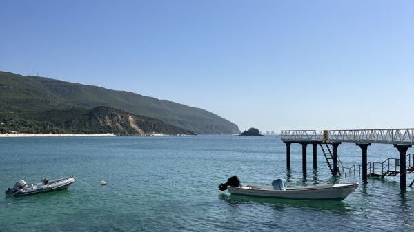 Two boats near a pier with a hillside and clear sky in the background.