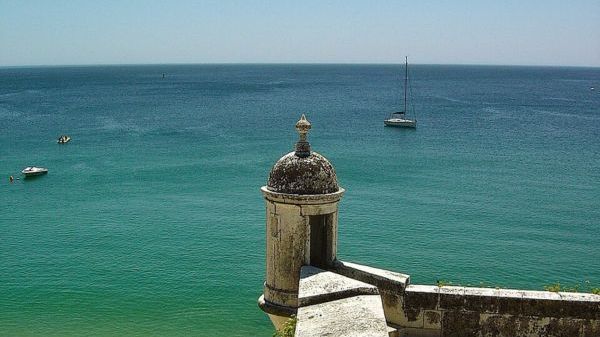 Seaside fort turret overlooking calm ocean with anchored boats.