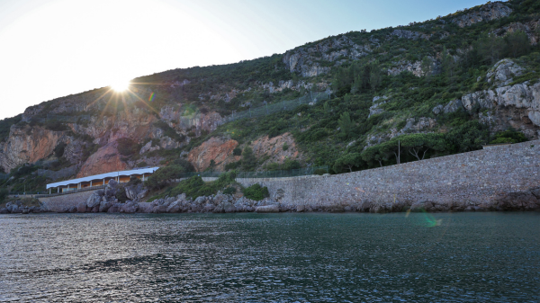 Sun setting over hills by a stone wall and water.