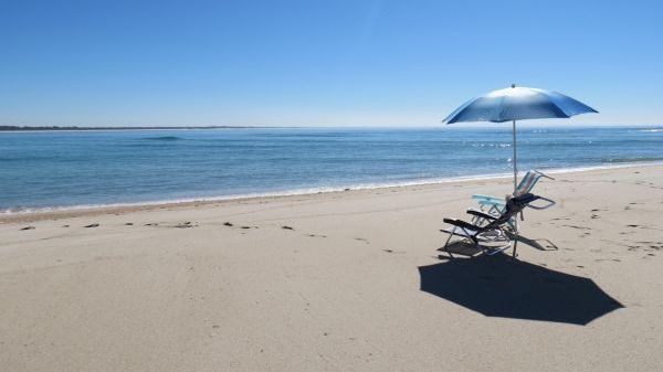 Chairs and umbrella on a sandy beach by the calm sea under a clear blue sky.