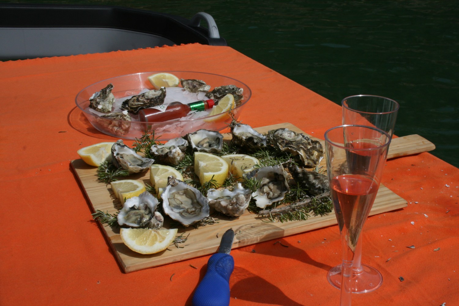 Oysters and lemon slices on a board, with a red drink in champagne glasses.